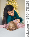 Mother hugs daughter by the Christmas tree during the holiday season 140478126