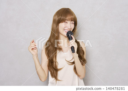 Middle-aged woman singing with a microphone, portrait, gray background Middle-aged woman singing with a microphone, portrait, gray background 140478281