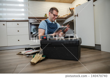 Handyman using digital tablet while repairing kitchen cabinet 140478740