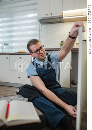 Handyman assembling kitchen cabinet in modern home kitchen Handyman assembling kitchen cabinet in modern home kitchen 140478742