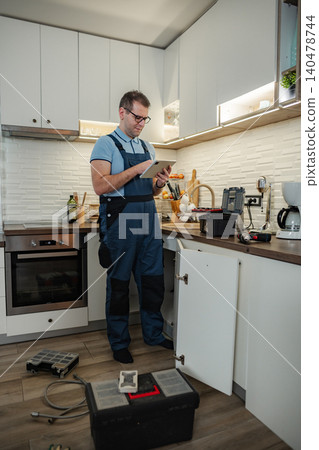 Plumber using digital tablet checking kitchen sink repair 140478744