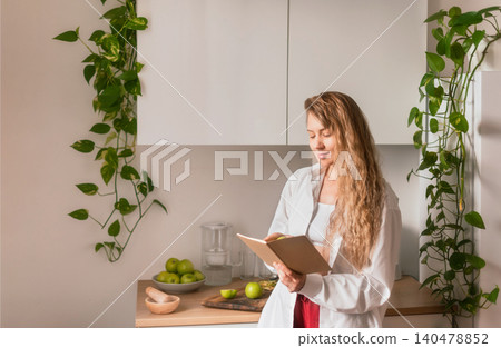 Woman Reading Recipe Book in Kitchen Woman Reading Recipe Book in Kitchen 140478852