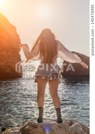 Sunset woman ocean standing on rocky shore facing golden horizon during a peaceful summer travel moment Sunset woman ocean standing on rocky shore facing golden horizon during a peaceful summer travel moment 140478995