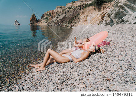 Summer beach vacation woman and child lying on pebble shore by the turquoise sea with mountains in background Summer beach vacation woman and child lying on pebble shore by the turquoise sea with mountains in background 140479311
