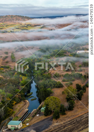 Vertical Aerial image of the Glenbawn Dam wall with morning fog drifting through the surrounding valley in NSW Australia. Drone photograph captures the reservoir, rugged mountain landscape Vertical Aerial image of the Glenbawn Dam wall with morning fog drifting through the surrounding valley in NSW Australia. Drone photograph captures the reservoir, rugged mountain landscape 140479539