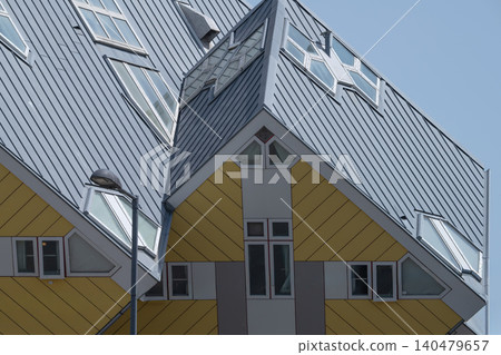 Close-up fragment of the iconic yellow Cube Houses in Rotterdam with angular geometric walls, windows and blue sky. 140479657