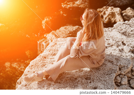 Woman cliff sunset young woman in beige knitwear sits on a rocky cliff by the sea at golden hour enjoying solitude Woman cliff sunset young woman in beige knitwear sits on a rocky cliff by the sea at golden hour enjoying solitude 140479666