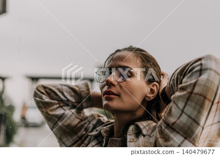 Woman rain glasses standing outdoors wearing plaid shirt with closed eyes enjoying refreshing droplets during a stormy day Woman rain glasses standing outdoors wearing plaid shirt with closed eyes enjoying refreshing droplets during a stormy day 140479677