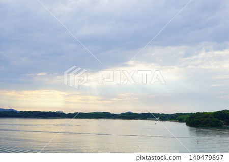 A fantastical lakeside landscape photograph featuring the expansive lake surface and light filtering through the clouds. 140479897