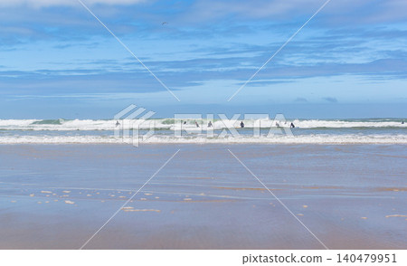 Surfers catching rolling waves on a wide, sunny beach under a vast blue sky. Inspires a feeling of freedom, active lifestyle, and coastal serenity. Perfect for travel and wellness. Surfers catching rolling waves on a wide, sunny beach under a vast blue sky. Inspires a feeling of freedom, active lifestyle, and coastal serenity. Perfect for travel and wellness. 140479951