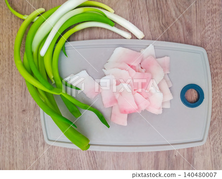 Sliced cured pork fat and fresh green onions served on a gray cutting board over wooden table. Perfect rustic food shot for traditional culinary blogs, menus, and cooking recipes. Sliced cured pork fat and fresh green onions served on a gray cutting board over wooden table. Perfect rustic food shot for traditional culinary blogs, menus, and cooking recipes. 140480007