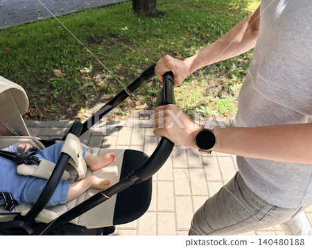 a mother pushing a baby stroller along a paved walkway. The baby's bare feet and legs are visible 140480188