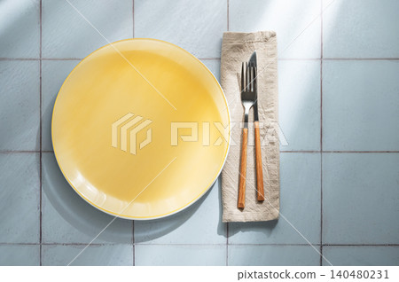 An empty yellow plate with a fork, knife and napkin on a blue tile background 140480231