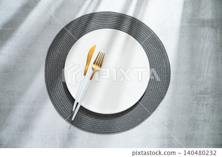 An empty white plate with a fork, knife and dark placemat on a gray concrete background An empty white plate with a fork, knife and dark placemat on a gray concrete background 140480232