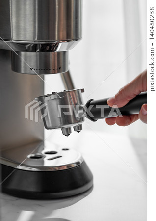 A hand holding a portafilter with freshly roasted coffee beans next to an espresso machine 140480238