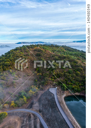 Aerial vertical image of the Glenbawn Dam wall meeting the surrounding mountain landscape surrounded by morning fog in NSW Australia. Drone photograph captures atmospheric low cloud Aerial vertical image of the Glenbawn Dam wall meeting the surrounding mountain landscape surrounded by morning fog in NSW Australia. Drone photograph captures atmospheric low cloud 140480349