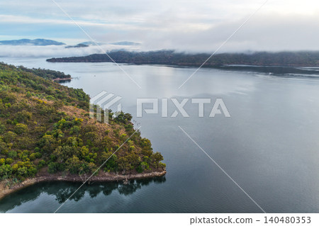 Aerial image of Glenbawn Dam and the surrounding mountain landscape with morning fog in NSW Australia. Drone photograph captures the expansive reservoir, rugged inland scenery Aerial image of Glenbawn Dam and the surrounding mountain landscape with morning fog in NSW Australia. Drone photograph captures the expansive reservoir, rugged inland scenery 140480353