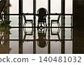 a triad of elegant bistro chairs stands silhouetted against a vast expanse of floor-to-ceiling windows, their patterned forms and the structural lines of the glass perfectly mirrored upon the 140481032