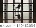 A solitary woven chair stands silhouetted against an expansive window, its crisp, geometric form mirrored perfectly across the polished expanse of a glossy floor. 140481034