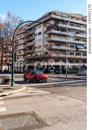 Car driving on the road near a building in an urban area during the daytime Car driving on the road near a building in an urban area during the daytime 140481176