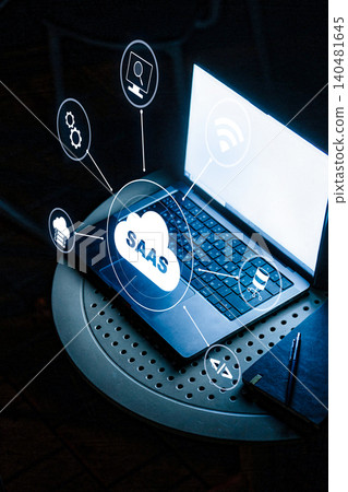 Saas symbols and concepts around an open laptop on a table during late evening hours Saas symbols and concepts around an open laptop on a table during late evening hours 140481645
