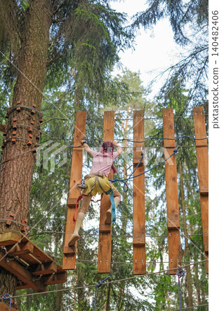 A girl climbs a curtain wall in an extreme sports park with safety gear. A girl climbs a curtain wall in an extreme sports park with safety gear. 140482406