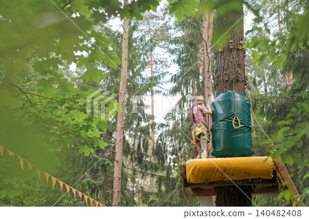 A girl is standing on a bridge at the top of a tree, preparing to bungee walk A girl is standing on a bridge at the top of a tree, preparing to bungee walk 140482408