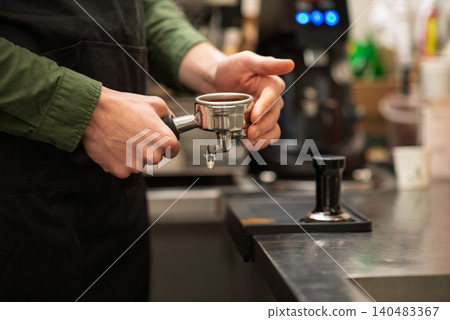 A close up of a barista holding a portafilter filled with coffee grounds A close up of a barista holding a portafilter filled with coffee grounds 140483367