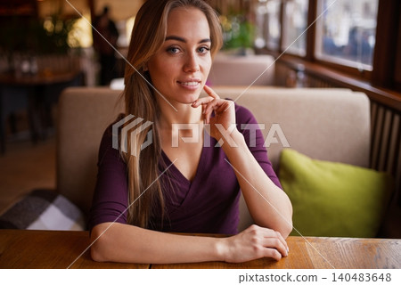 Beautiful blonde woman looking directly at the camera while sitting inside a cozy cafe 140483648