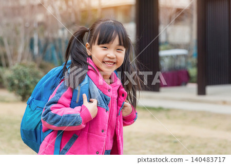 Happy Asian schoolgirl carrying a blue backpack walking home after school in the park Happy Asian schoolgirl carrying a blue backpack walking home after school in the park 140483717