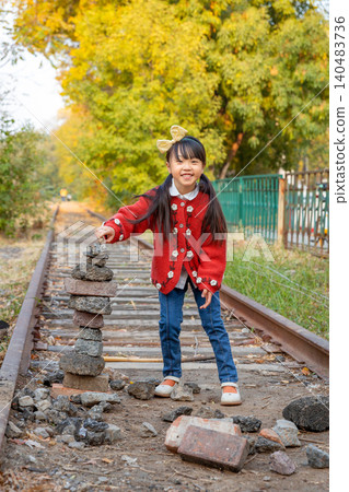 Curious little girl looks at a stack of balanced stones next to an old railway track in nature. Curious little girl looks at a stack of balanced stones next to an old railway track in nature. 140483736