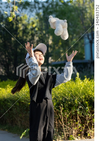 A young girl catching a white plush bear toy thrown in the air outside. A young girl catching a white plush bear toy thrown in the air outside. 140483752