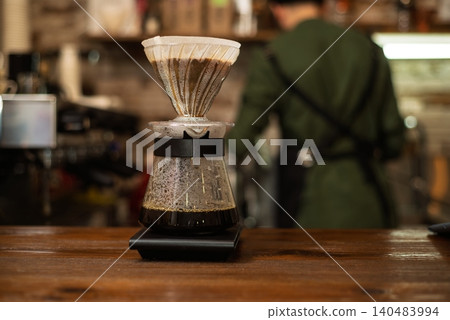 A glass coffee server with a dripper on a scale at a bar counter A glass coffee server with a dripper on a scale at a bar counter 140483994