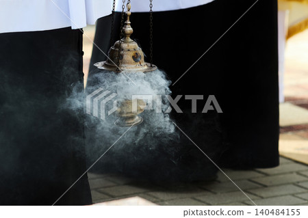 Priest holding censer swinging incense smoke during ritual Priest holding censer swinging incense smoke during ritual 140484155