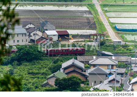 A rural landscape viewed from the top of a mountain and the maroon-colored train of the Yoro Railway. A rural landscape viewed from the top of a mountain and the maroon-colored train of the Yoro Railway. 140484564