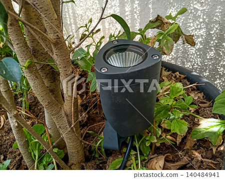 Modern Black LED Garden Spike Spotlight for Landscape Lighting adjustable black LED spike light installed in garden soil near a tree. Modern Black LED Garden Spike Spotlight for Landscape Lighting adjustable black LED spike light installed in garden soil near a tree. 140484941