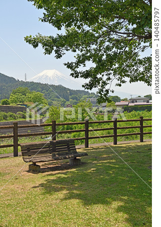 A wooden bench in Katsuragawa Park: A luxurious and special spot to relax, offering a beautiful view of snow-capped Mount Fuji from the shade of the lush green trees. A wooden bench in Katsuragawa Park: A luxurious and special spot to relax, offering a beautiful view of snow-capped Mount Fuji from the shade of the lush green trees. 140485797