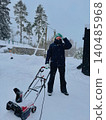 man clearing snow near wooden house in countryside using electric snow blower 140485968