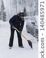man shoveling snow with a shovel on the driveway of his countryside property during a snowfall 140485971