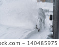 man clearing snow near wooden house in countryside using electric snow blower 140485975