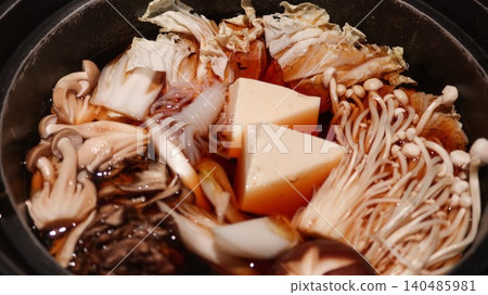 close up of a Japanese sukiyaki shabu shabu hot pot with simmering mushrooms, Enoki mushrooms, napa cabbage and tofu in a dark broth in a black pot with copy space close up of a Japanese sukiyaki shabu shabu hot pot with simmering mushrooms, Enoki mushrooms, napa cabbage and tofu in a dark broth in a black pot with copy space 140485981