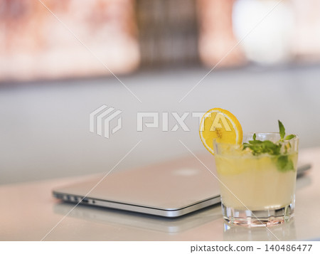 a glass of cocktail and laptop on a bar table a glass of cocktail and laptop on a bar table 140486477
