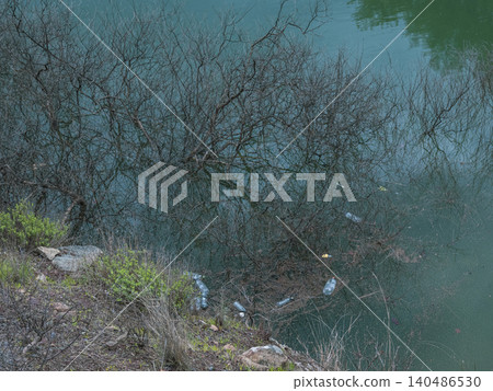 pollution in nature: plastic bottles and garbage floating near a forest lake pollution in nature: plastic bottles and garbage floating near a forest lake 140486530