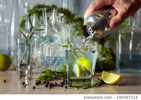 Gin and tonic cocktail is poured from a shaker into a glass with ice and lime wedges. Gin and tonic cocktail is poured from a shaker into a glass with ice and lime wedges. 140487214