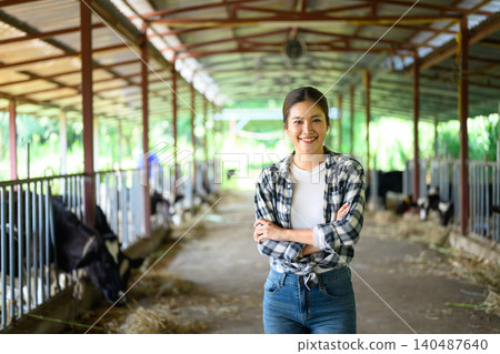 Female farmer standing in dairy barn with cows, confident agriculture worker Female farmer standing in dairy barn with cows, confident agriculture worker 140487640