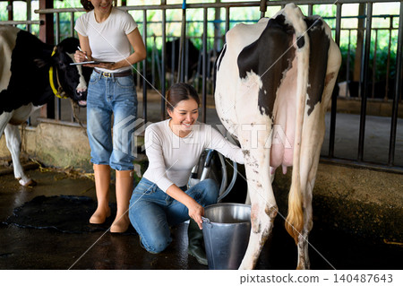 Dairy workers monitoring milking process and recording data in cow barn Dairy workers monitoring milking process and recording data in cow barn 140487643