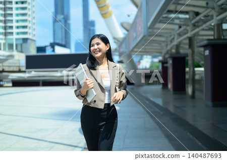 Businesswoman with holding laptop looking up in urban cityscape Businesswoman with holding laptop looking up in urban cityscape 140487693