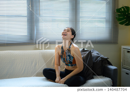 Woman relaxing on sofa after workout, feeling happy and calm in cozy home lifestyle Woman relaxing on sofa after workout, feeling happy and calm in cozy home lifestyle 140487704