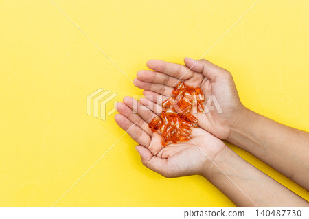 Hands cradle glowing orange capsules against bright yellow background. Soft lighting highlights each pill's glossy texture. Warm tone suggests health, wellness, or self-care Hands cradle glowing orange capsules against bright yellow background. Soft lighting highlights each pill's glossy texture. Warm tone suggests health, wellness, or self-care 140487730