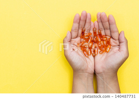 Hands cradle glowing orange capsules against bright yellow background. Soft lighting highlights each pill's glossy texture. Warm tone suggests health, wellness, or self-care Hands cradle glowing orange capsules against bright yellow background. Soft lighting highlights each pill's glossy texture. Warm tone suggests health, wellness, or self-care 140487731